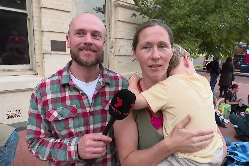 A couple being interviewed by a TV crew, the woman holding a toddler.