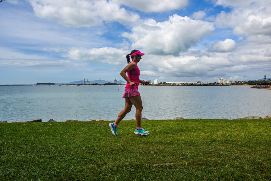 A woman running along grass near the coast.
