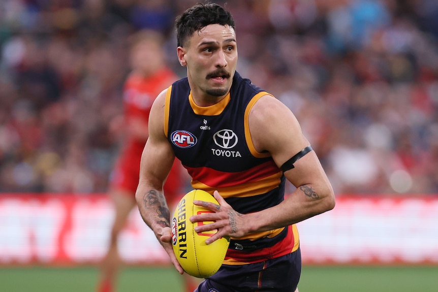 Izak Rankine holds the ball in two hands during a 2025 AFL match.