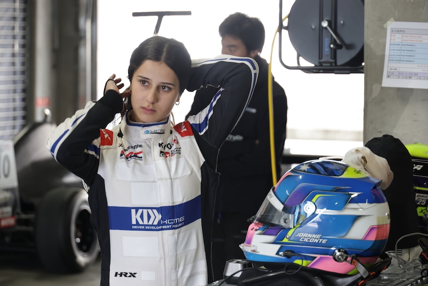 Female racer in the garage during a testing session, preparing to put on her helmet