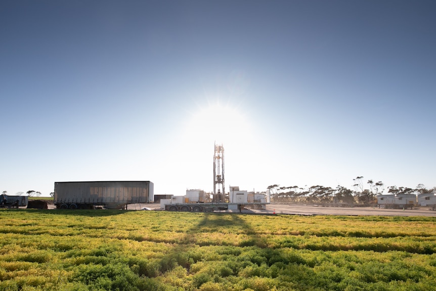 A drill rig with the sun behind it and grass in front of it