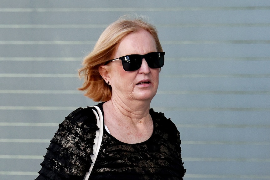 A middle aged woman wearing dark sunglasses and a black tshirt.