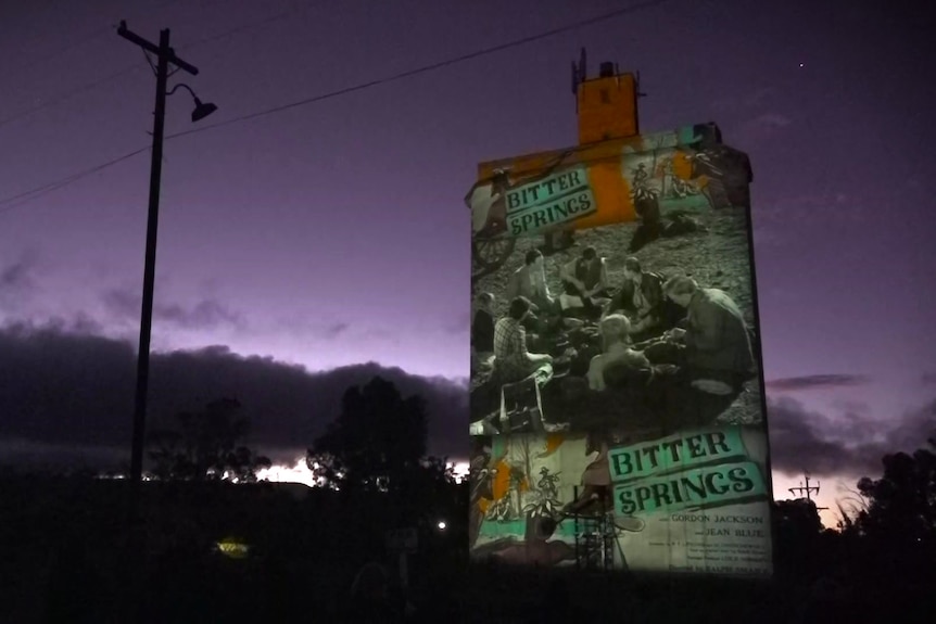A tall, industrial silo at sunset, with images projected onto it of a film.