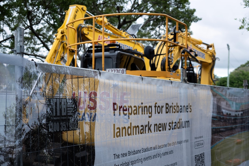 A large yellow excavator behind a fence.