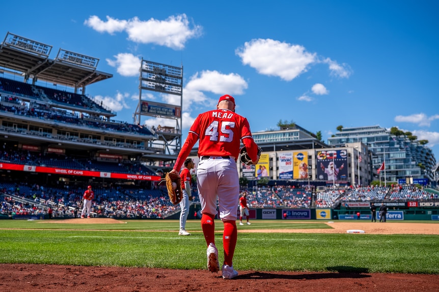 Curtis Mead, wearing red kit and with a pitcher mitt, on the field during a baseball game.