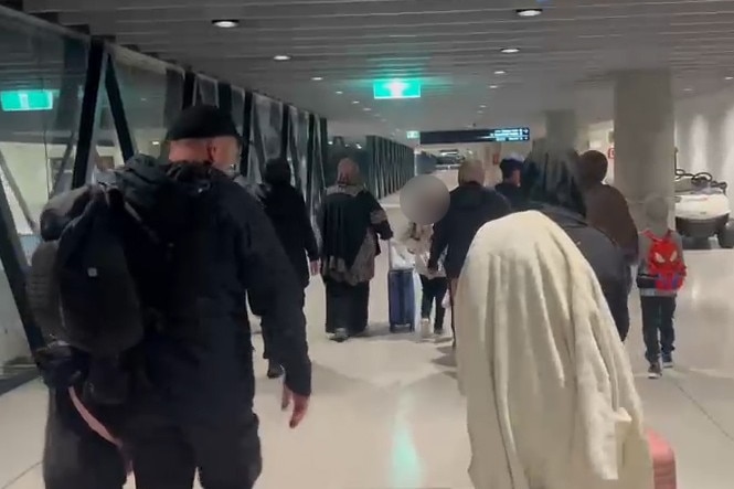 A group of people roll suitcases through an airport terminal