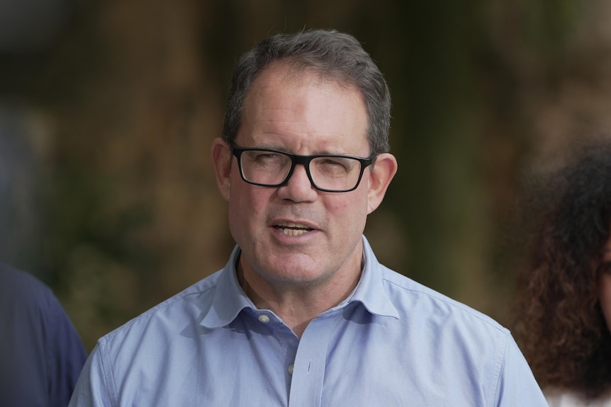 A man wearing a blue shirt talks to the media