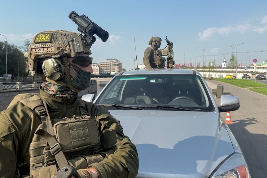 Two heavily armed soldiers looking on.