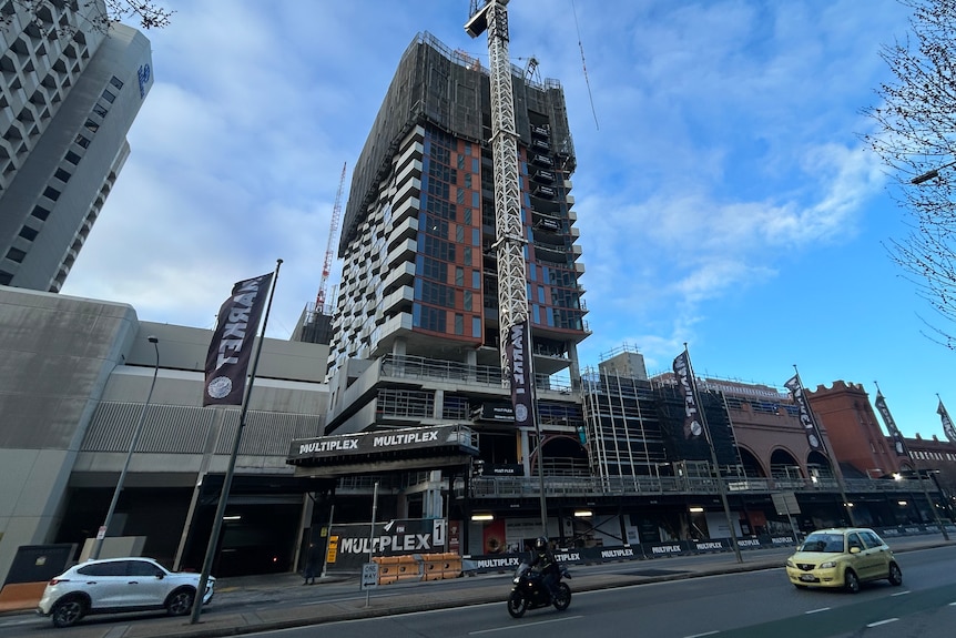 a building tower being erected with blue sky in background and cars on road in front