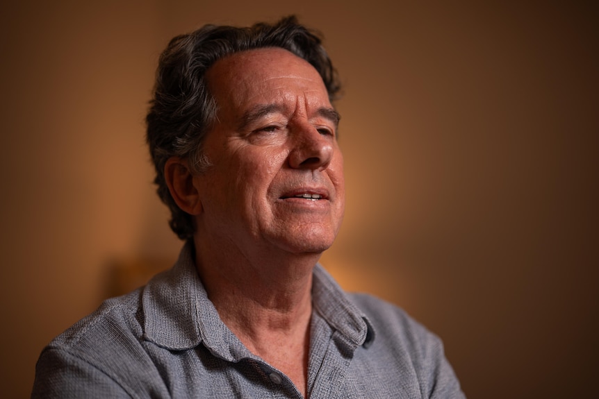 Man in collard shirt looks away from camera in a dimly lit room