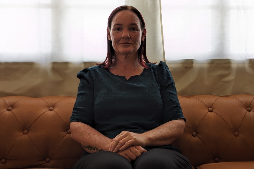 A woman sits on a couch with hands clasped.
