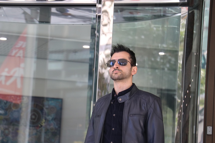 A man wearing sunglasses stands outside a courtroom