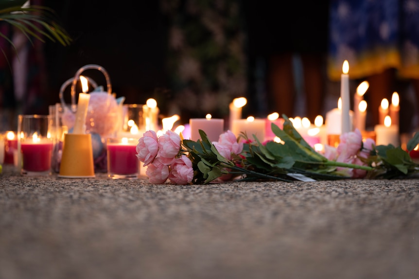 A pink flower resting on the ground, colourful candles are burning nearby.