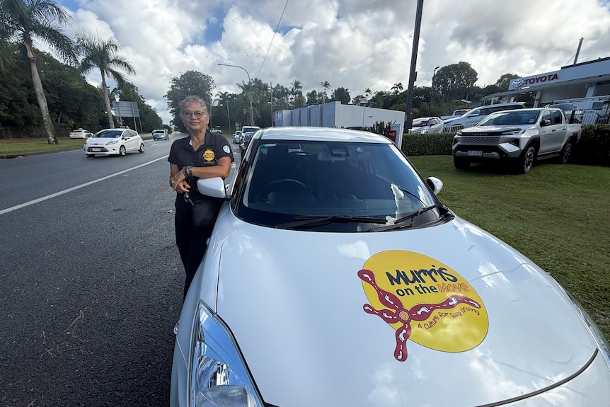 Woman standing beside white car on busy road.