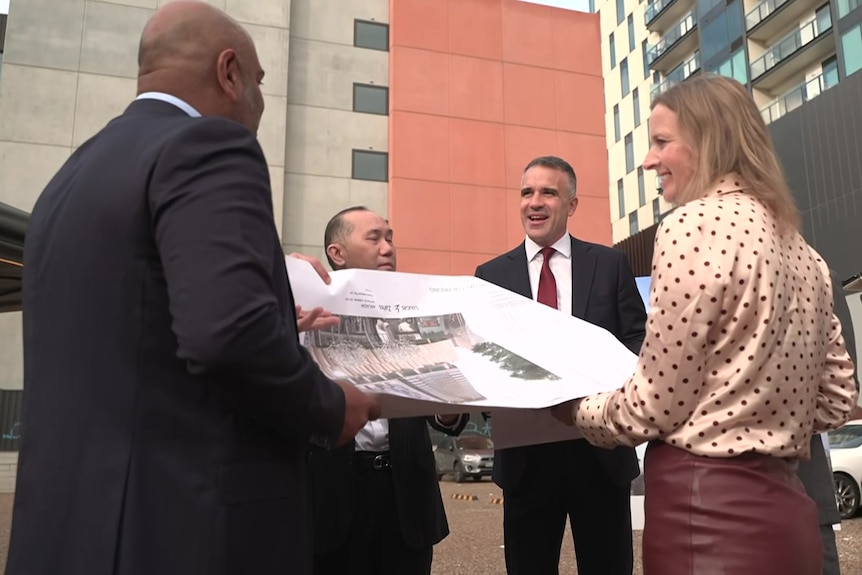 A group of people looking at a large piece of paper near city buildings