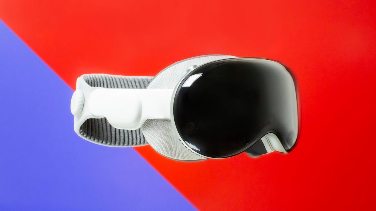 Apple Vision Pro AR/VR headset is shown on a split background of purple and red.