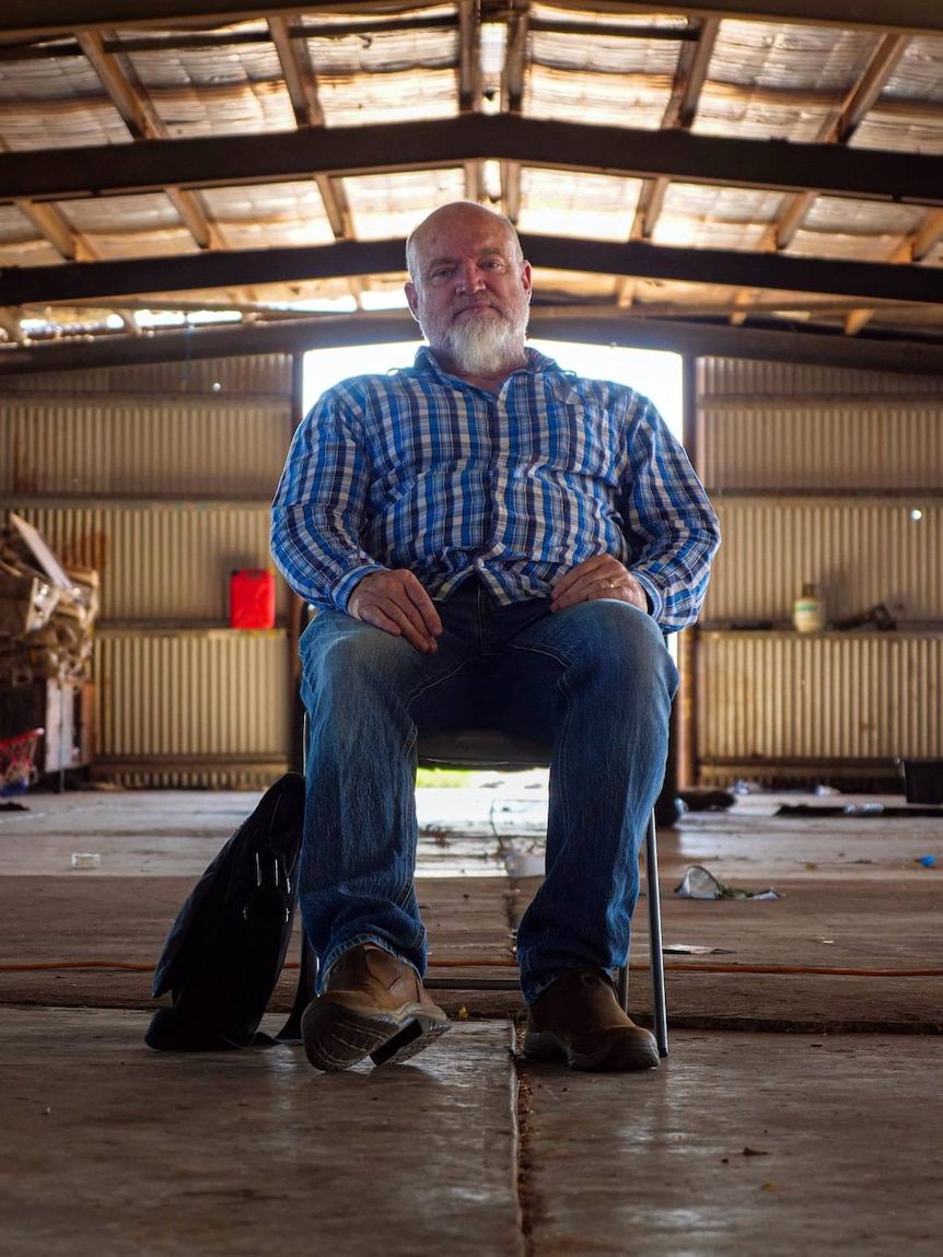 A wide angle shot of an older white man sitting alone in a large shed.