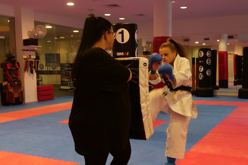 A girl in a white karate outfit in action as a woman blocks her kick.