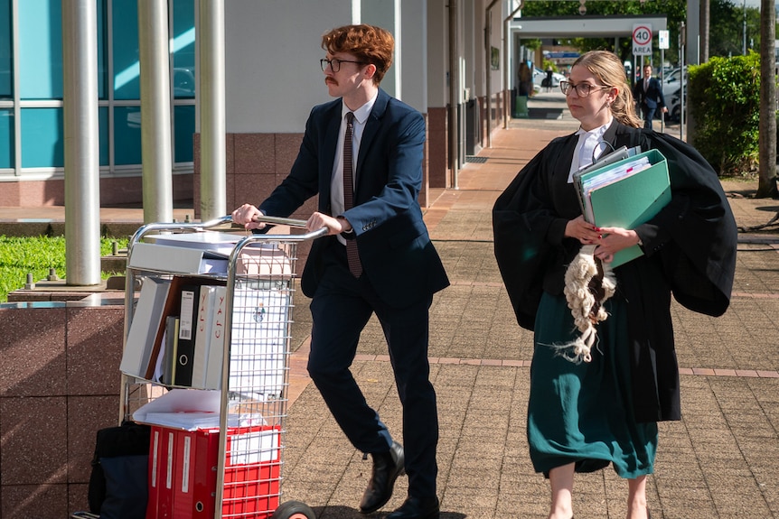 Two lawyers walking on footpath, one pushing a trolley full of documents, the other dressed in robes