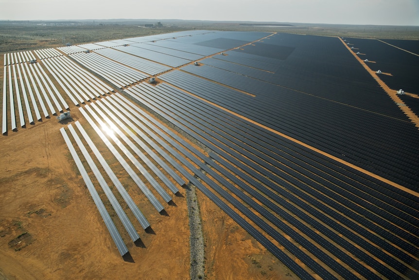 A drone photo of a large collection of solar panels in several rows in an outback landscape