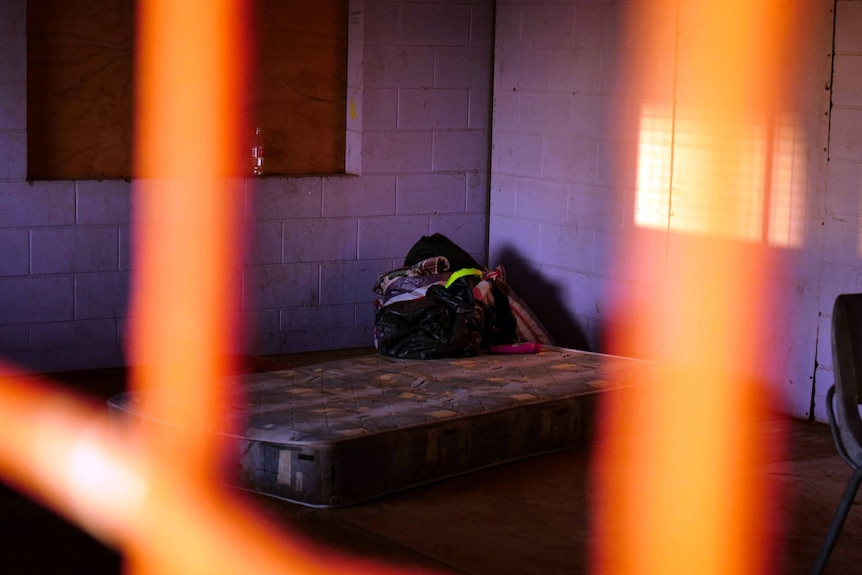 A bare matteress with a rubbish bag full of personal belongings, pictured through a window grate.