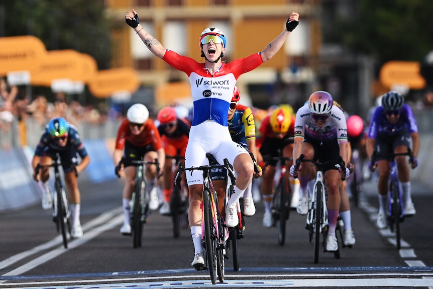 Lorena Wiebes holds up her hands in victory while cycling.