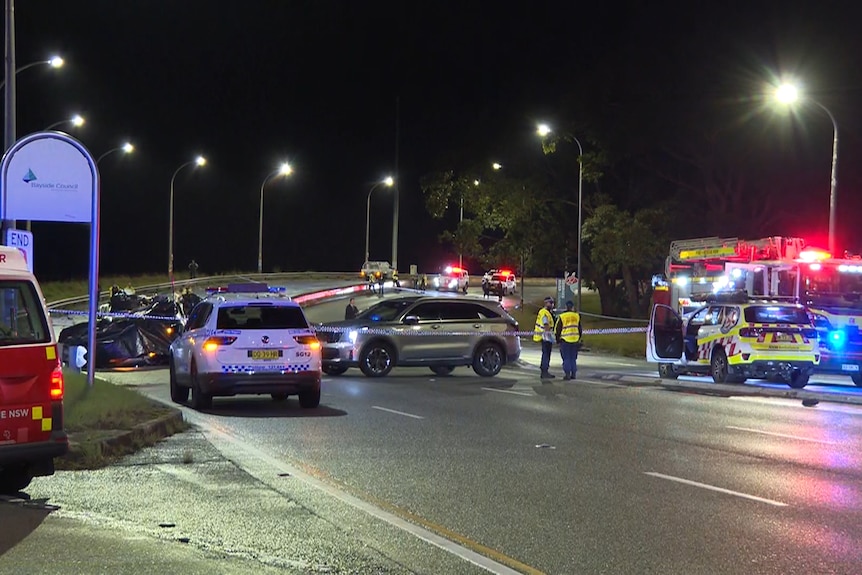 Emergency vehicles with flashing lights parked on a road near a crashed car.