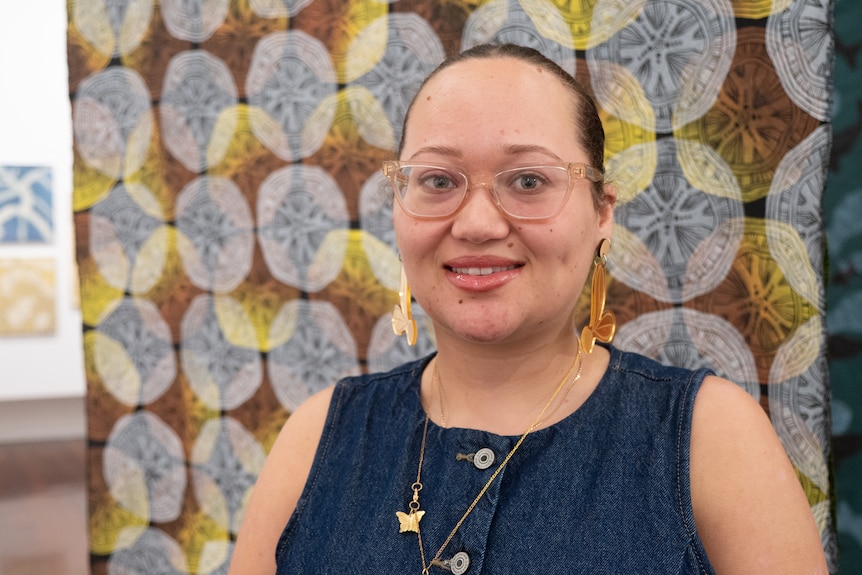 Young woman in glasses and denim top stands in front of printed fabric panel