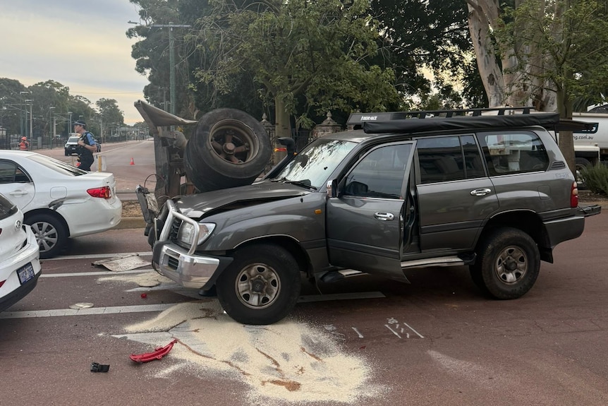 A damaged car sitting near train lines.