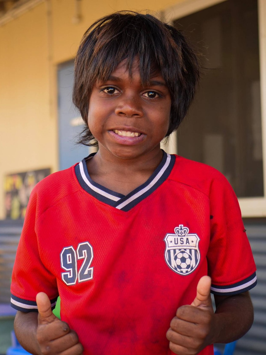 A boy smiles in a red t-shirt.