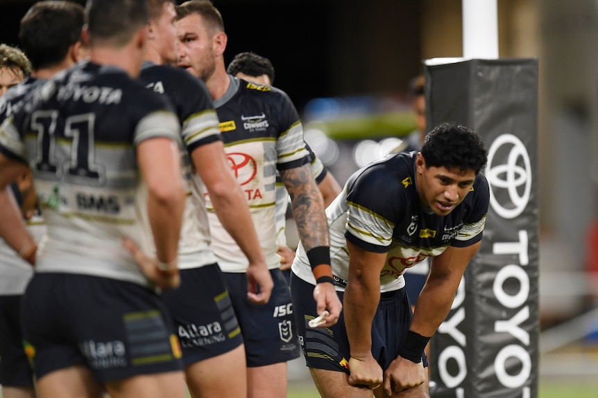 Jason is slumped over during a rugby league match, other teammates stand around in black and white. Toyota sign.