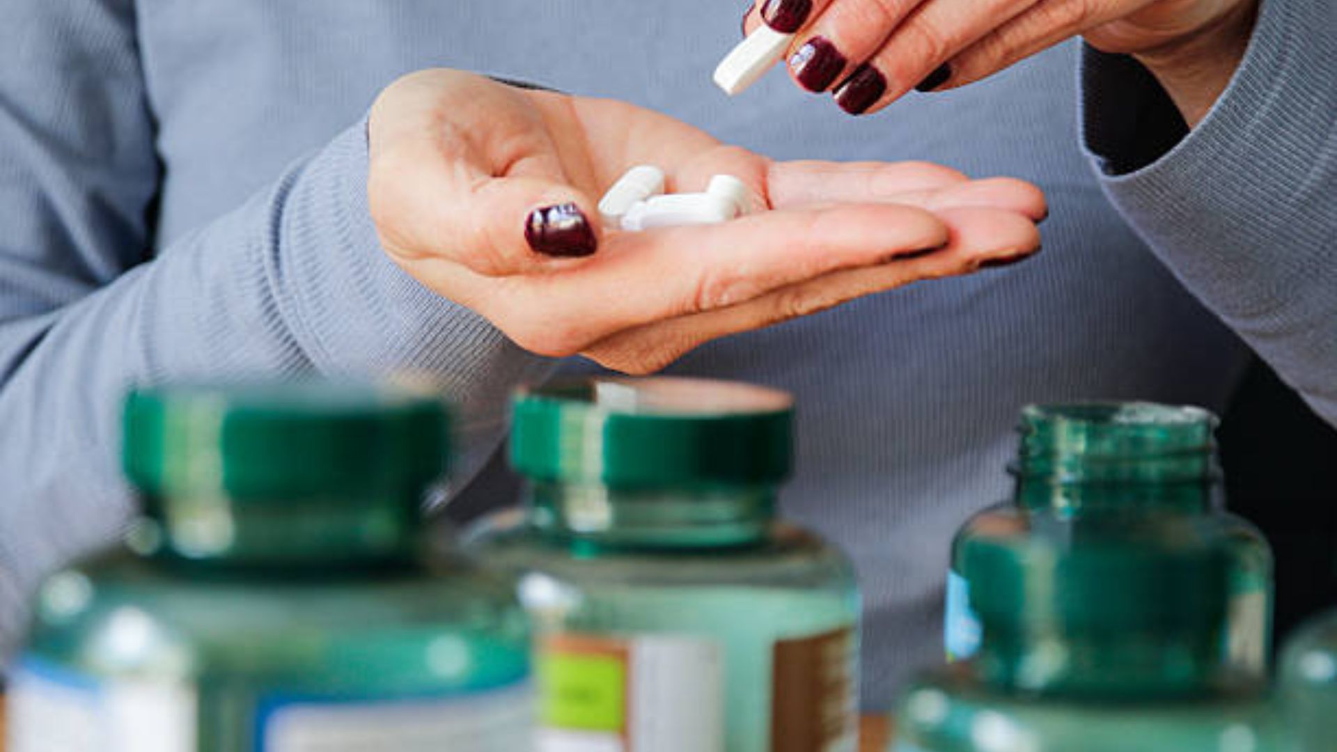 A woman's manicured hand holds a handful of white multivitamin supplements.
