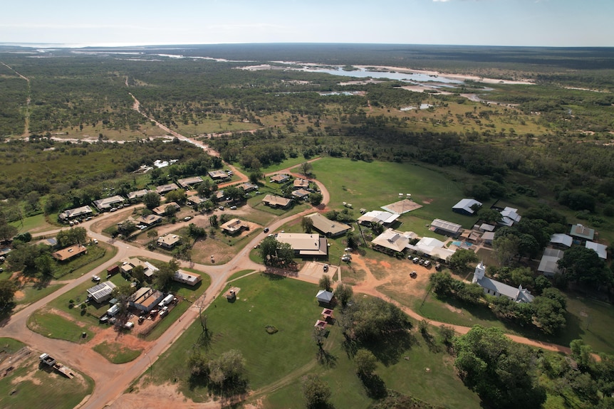 Aerial of about 30 buildings surrounded by green grass and creek in background