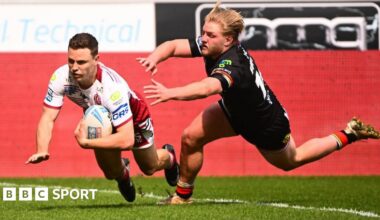 Wigan Warriors full-back Jai Field, in white and red, dives over the line to score a try as a Bradford player tries to tackle him