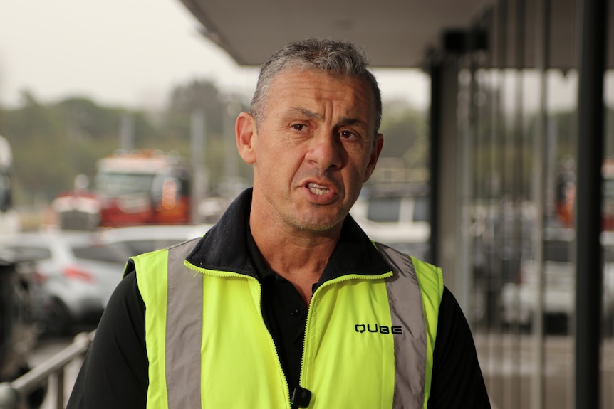 Paul speaks while wearing a yellow high vis vest.