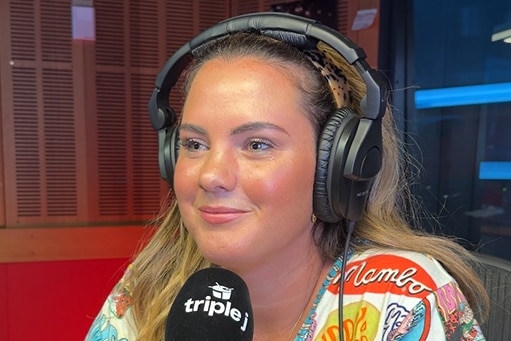 A woman wearing a brightly coloured t-shirt and headphones, talking into a microphone.