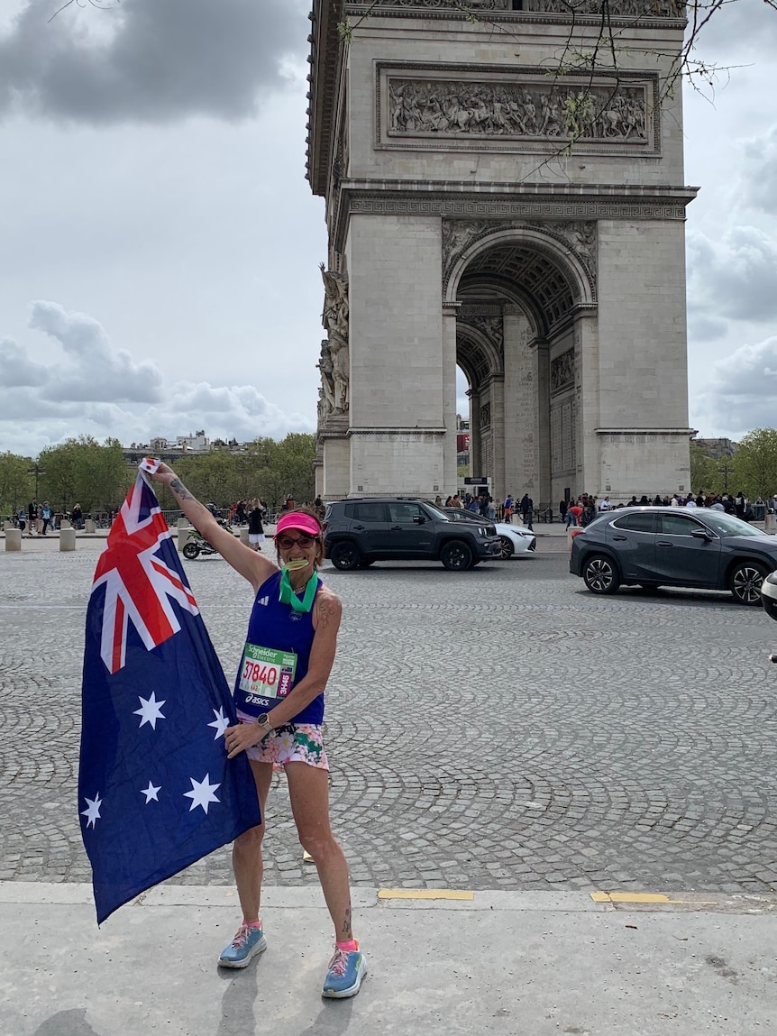 A woman standing on a French street holding an Australian flag and biting a medal.