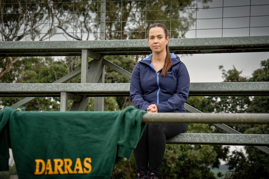A woman sits in a grandstand in front of a jumper that says "Darras".