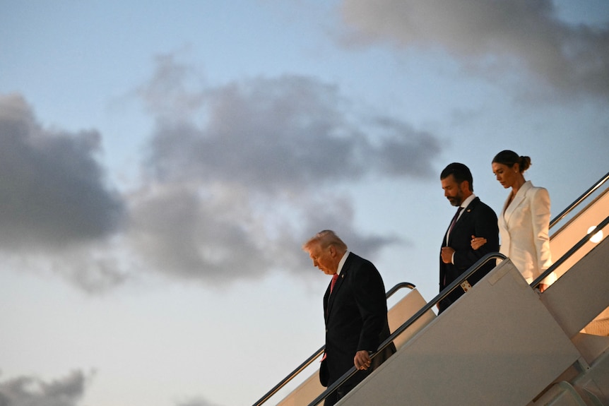 Three people walk down the stairs of a plane.
