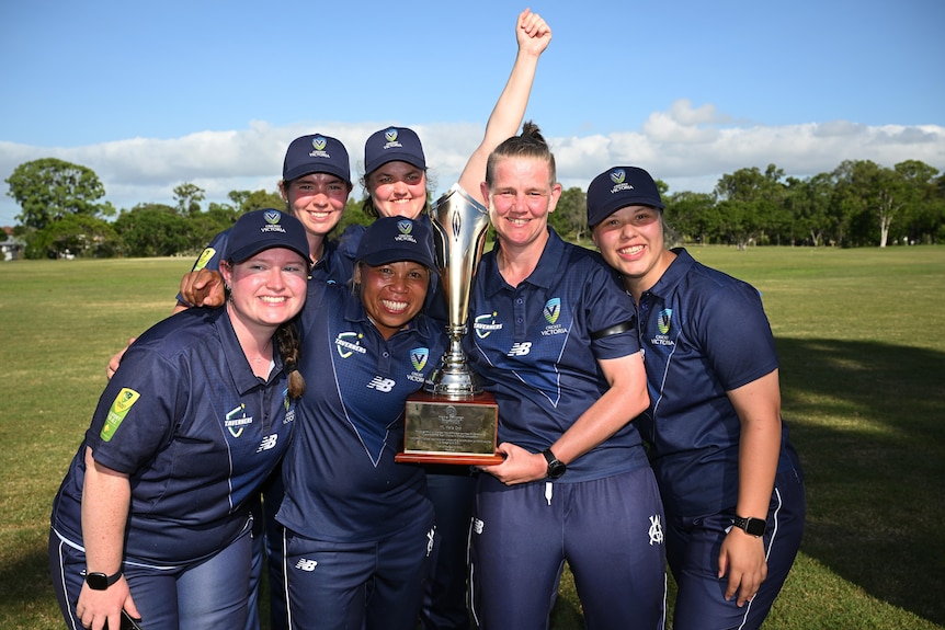 Players from Victoria's women's Deaf cricket team hold a trophy and smile broadly