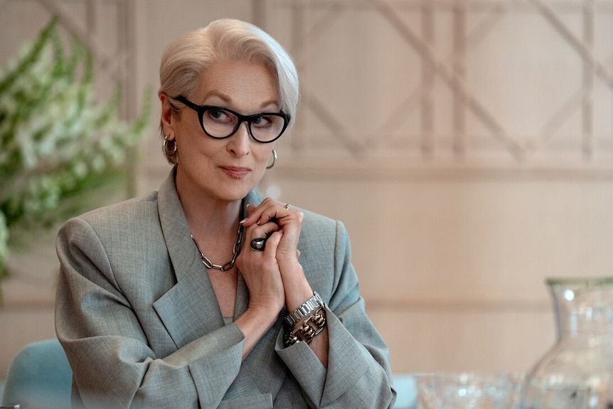An older woman in a jacket and glasses smiles