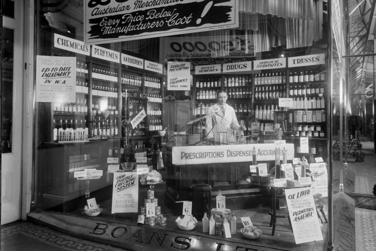 Black and white photo of pharmacy shop with counter and many shelves of bottles
