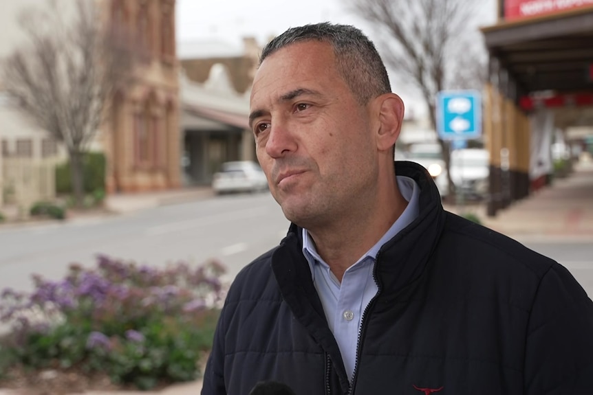 A man in front of a quiet country road with a blue collared shirt and a jacket