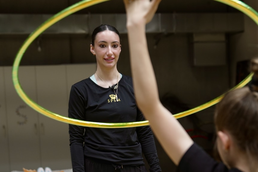 A young woman with black hair looks on as her student throws a hula hoop.