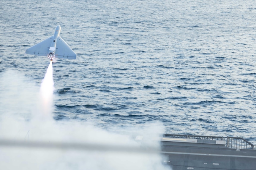A drone launches from the flight deck of a war ship at sea.