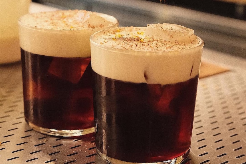 Two cups of coffee beverages with orange zest falling on top of them.