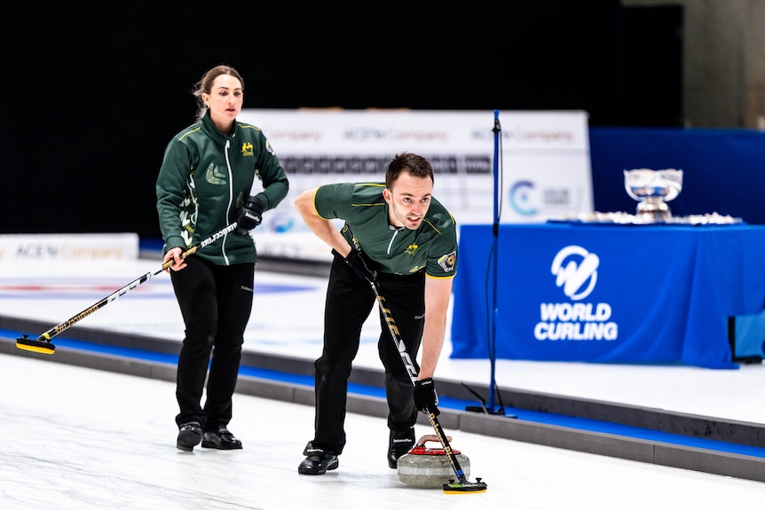 Dean Hewitt sweeps as Tahli Gill watches during curling championship.