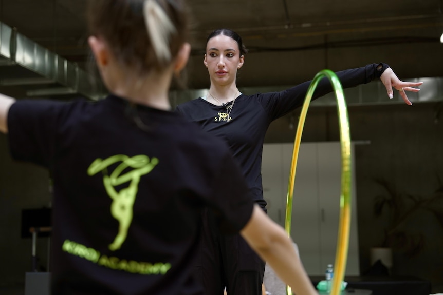 A young woman hangs a hula hoop on her arm and holds it out to show a student.