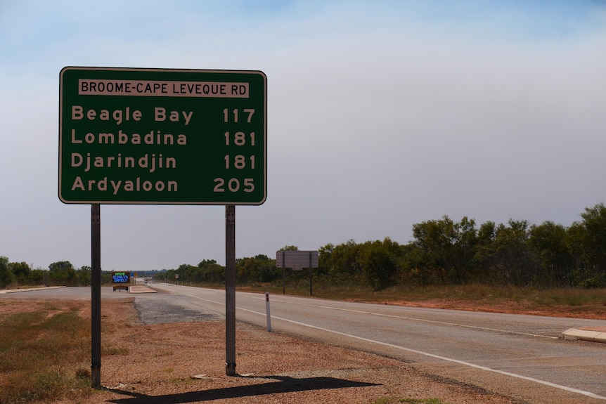 Green street sign on red dirt and bitumen road