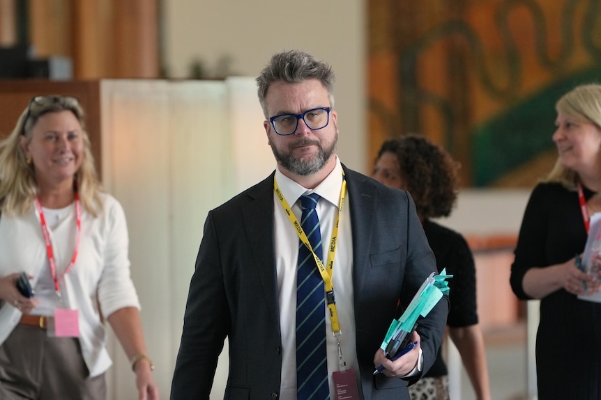 A man in a suit walks with other people behind him.